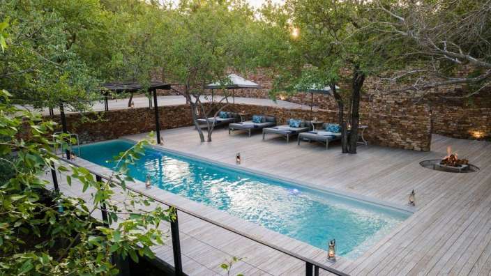 Ein großer Swimmingpool mit einem Holzdeck umgeben von Bäumen