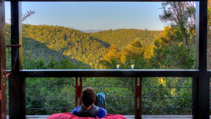 Ein Mann sitzt auf einem Balkon mit Blick auf einen Wald
