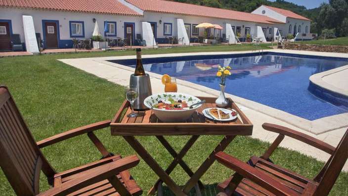 Ein Tisch mit einem Tablett mit Essen und einer Flasche Wein neben einem Swimmingpool