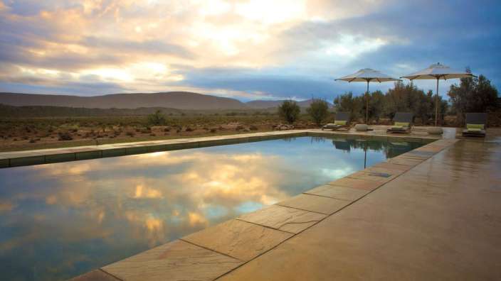 Ein Swimmingpool mit Sonnenschirmen und Liegestühlen im Hintergrund