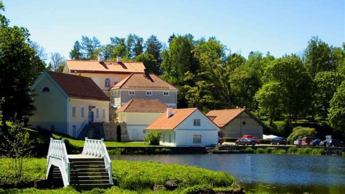 Eine kleine weiße Brücke führt zu einem großen weißen Haus mit roten Dächern