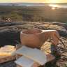 Eine Tasse Kaffee steht auf einem Felsen neben einem Stück Brot und Käse