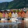 Die bunten Hansehäuser von Bryggen in Bergen spiegeln sich im Wasser, während Yachten und ein Motorboot im Hafen liegen.