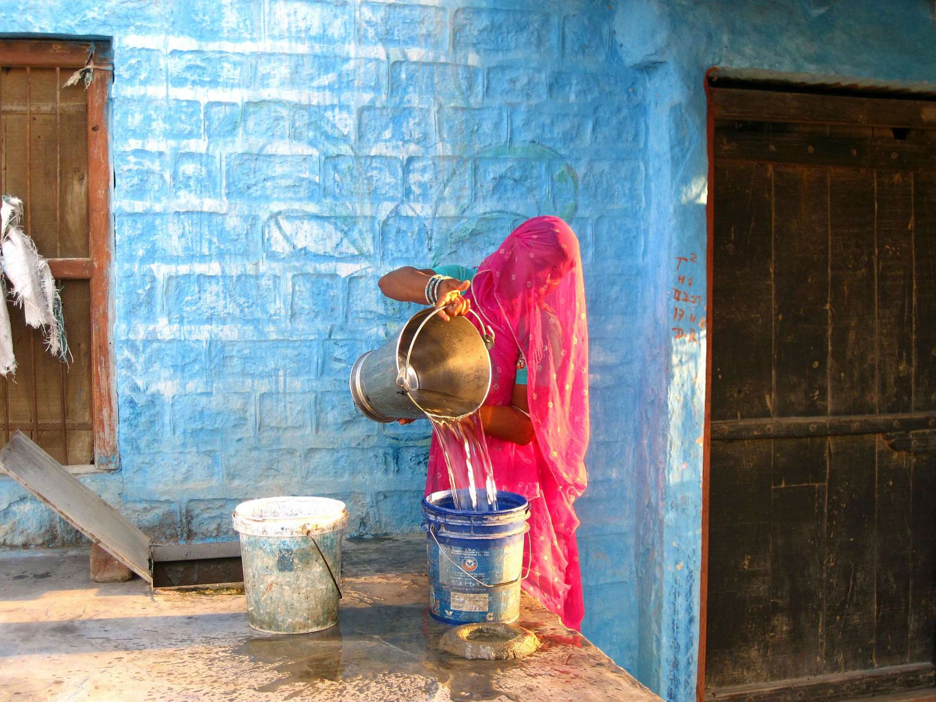 Eine Frau gießt Wasser aus einem Eimer in einen blauen Eimer