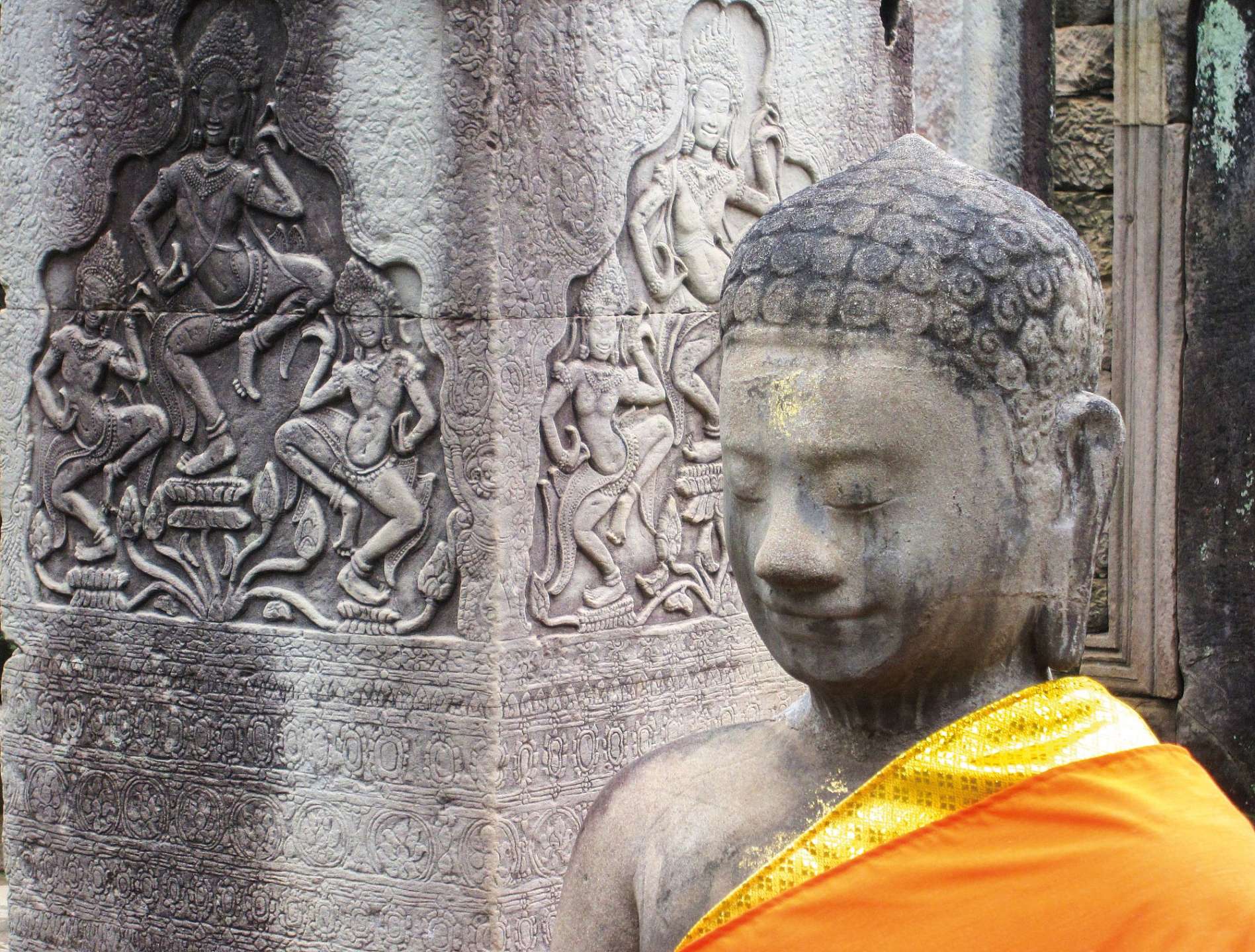 Eine buddhistische Statue steht vor einem Steinrelief