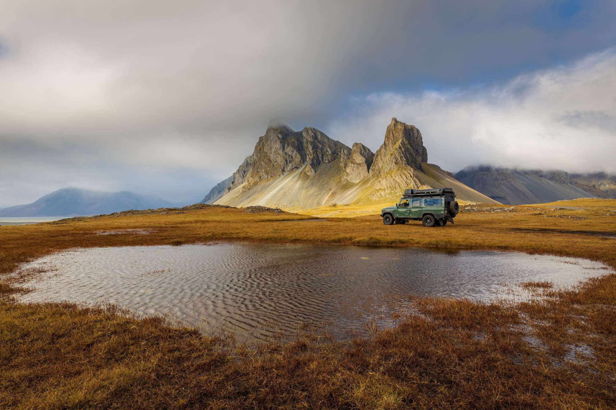 Ein grüner jeep steht neben einem kleinen teich mit einem berg im hintergrund